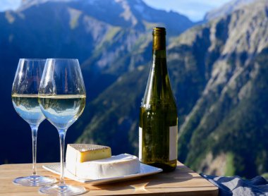 Fransa 'nın Savoy bölgesinden lezzetli peynir ve şarap, tomme ve reblochon de savoie peynirleri ve yazın açık havada sunulan beyaz şarap arka planda Alp dağları zirveleri