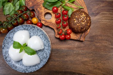 Peynir koleksiyonu, beyaz İtalyan peynirli mozzarella topları, kırmızı vişneli domates ve taze fesleğen yapraklarıyla servis ediliyor.