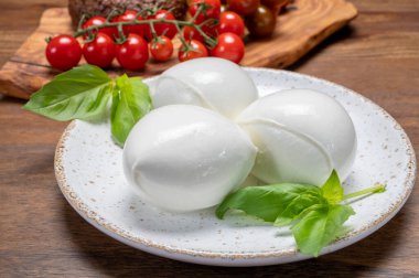 Peynir koleksiyonu, beyaz İtalyan peynirli mozzarella topları, kırmızı vişneli domates ve taze fesleğen yapraklarıyla servis ediliyor.