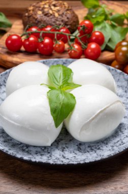 Peynir koleksiyonu, beyaz İtalyan peynirli mozzarella topları, kırmızı vişneli domates ve taze fesleğen yapraklarıyla servis ediliyor.