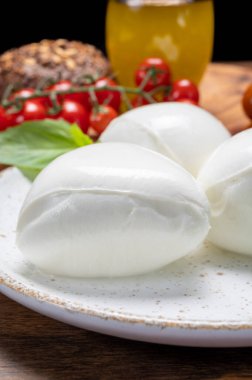 Peynir koleksiyonu, beyaz İtalyan peynirli mozzarella topları, kırmızı vişneli domates ve taze fesleğen yapraklarıyla servis ediliyor.