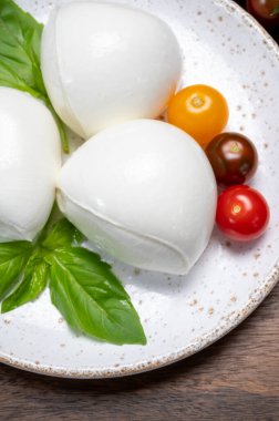 Peynir koleksiyonu, beyaz İtalyan peynirli mozzarella topları, kırmızı vişneli domates ve taze fesleğen yapraklarıyla servis ediliyor.
