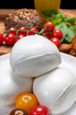 Peynir koleksiyonu, beyaz İtalyan peynirli mozzarella topları, kırmızı vişneli domates ve taze fesleğen yapraklarıyla servis ediliyor.