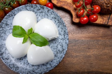 Peynir koleksiyonu, beyaz İtalyan peynirli mozzarella topları, kırmızı vişneli domates ve taze fesleğen yapraklarıyla servis ediliyor.