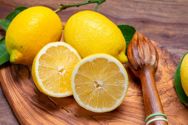 Taze taze sarı İtalyan limonları ve ahşap sıkacağı, zeytin ağacı arka planında yeni hasat.