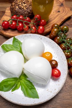 Peynir koleksiyonu, beyaz İtalyan peynirli mozzarella topları, kırmızı vişneli domates ve taze fesleğen yapraklarıyla servis ediliyor.
