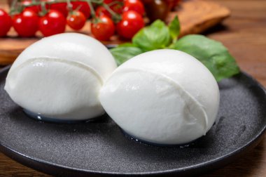 Peynir koleksiyonu, beyaz İtalyan peynirli mozzarella topları, kırmızı vişneli domates ve taze fesleğen yapraklarıyla servis ediliyor.
