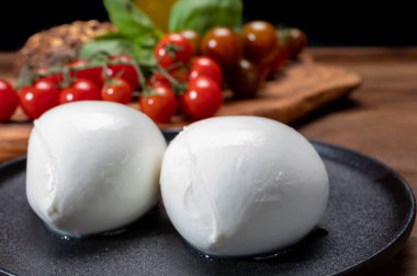 Peynir koleksiyonu, beyaz İtalyan peynirli mozzarella topları, kırmızı vişneli domates ve taze fesleğen yapraklarıyla servis ediliyor.
