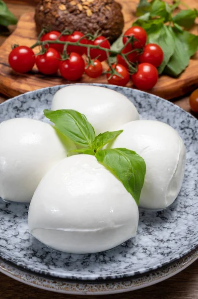 Peynir koleksiyonu, beyaz İtalyan peynirli mozzarella topları, kırmızı vişneli domates ve taze fesleğen yapraklarıyla servis ediliyor.