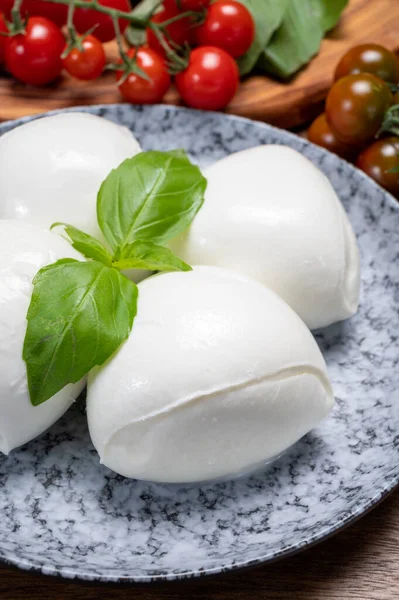 Peynir koleksiyonu, beyaz İtalyan peynirli mozzarella topları, kırmızı vişneli domates ve taze fesleğen yapraklarıyla servis ediliyor.
