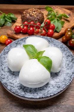 Peynir koleksiyonu, beyaz İtalyan peynirli mozzarella topları, kırmızı vişneli domates ve taze fesleğen yapraklarıyla servis ediliyor.