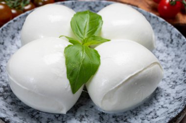 Peynir koleksiyonu, beyaz İtalyan peynirli mozzarella topları, kırmızı vişneli domates ve taze fesleğen yapraklarıyla servis ediliyor.