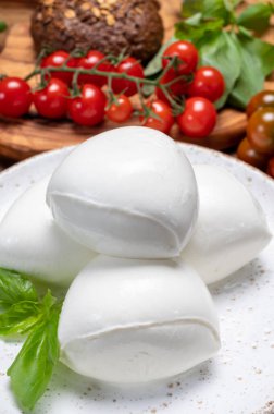 Peynir koleksiyonu, beyaz İtalyan peynirli mozzarella topları, kırmızı vişneli domates ve taze fesleğen yapraklarıyla servis ediliyor.