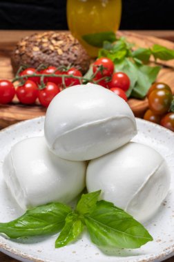 Peynir koleksiyonu, beyaz İtalyan peynirli mozzarella topları, kırmızı vişneli domates ve taze fesleğen yapraklarıyla servis ediliyor.