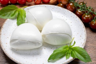 Peynir koleksiyonu, beyaz İtalyan peynirli mozzarella topları, kırmızı vişneli domates ve taze fesleğen yapraklarıyla servis ediliyor.