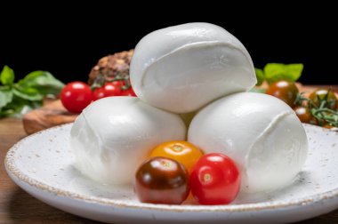 Peynir koleksiyonu, beyaz İtalyan peynirli mozzarella topları, kırmızı vişneli domates ve taze fesleğen yapraklarıyla servis ediliyor.