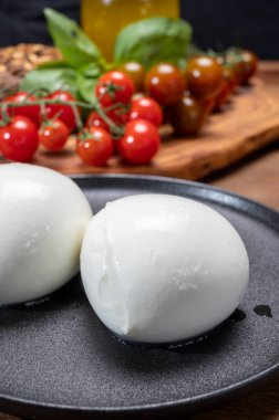 Peynir koleksiyonu, beyaz İtalyan peynirli mozzarella topları, kırmızı vişneli domates ve taze fesleğen yapraklarıyla servis ediliyor.