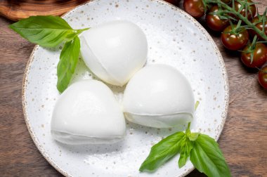 Peynir koleksiyonu, beyaz İtalyan peynirli mozzarella topları, kırmızı vişneli domates ve taze fesleğen yapraklarıyla servis ediliyor.