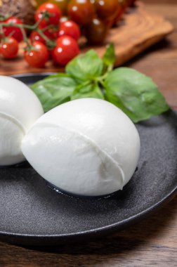 Peynir koleksiyonu, beyaz İtalyan peynirli mozzarella topları, kırmızı vişneli domates ve taze fesleğen yapraklarıyla servis ediliyor.
