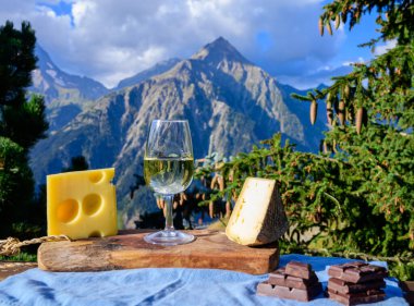 Bir bardak İsviçre viskisi ya da savoy beyaz şarap, tomme ve emmental peynir, güneşli bir günde arka planda Alp dağlarının zirveleri.