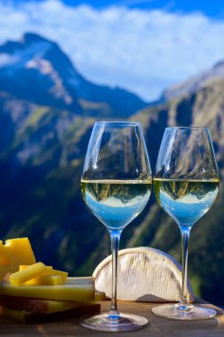 Fransa 'nın Savoy bölgesinden lezzetli peynir ve şarap, Beaufort, abondance, emmental, tomme ve reblochon de savoie peynirleri ve yazın açık havada sunulan beyaz şarap arka planda Alp dağlarının zirveleri
