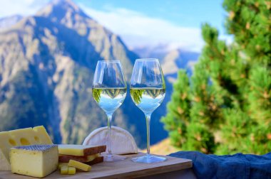 Fransa 'nın Savoy bölgesinden lezzetli peynir ve şarap, Beaufort, abondance, emmental, tomme ve reblochon de savoie peynirleri ve yazın açık havada sunulan beyaz şarap arka planda Alp dağlarının zirveleri