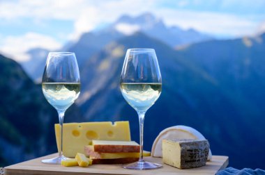Fransa 'nın Savoy bölgesinden lezzetli peynir ve şarap, Beaufort, abondance, emmental, tomme ve reblochon de savoie peynirleri ve yazın açık havada sunulan beyaz şarap arka planda Alp dağlarının zirveleri