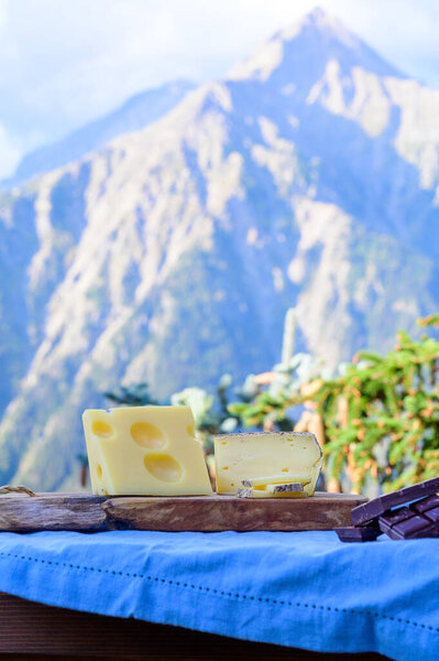 Tasty Swiss cheeses and dark pure chocolate, emmental, gruyere, appenzeller served outdoor with Alpine mountains peaks in summer on background