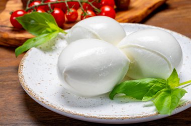 Peynir koleksiyonu, beyaz İtalyan peynirli mozzarella topları, kırmızı vişneli domates ve taze fesleğen yapraklarıyla servis ediliyor.