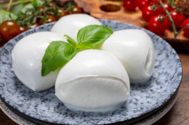 Peynir koleksiyonu, beyaz İtalyan peynirli mozzarella topları, kırmızı vişneli domates ve taze fesleğen yapraklarıyla servis ediliyor.