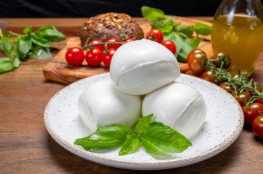 Peynir koleksiyonu, beyaz İtalyan peynirli mozzarella topları, kırmızı vişneli domates ve taze fesleğen yapraklarıyla servis ediliyor.