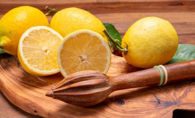 Taze taze sarı İtalyan limonları ve ahşap sıkacağı, zeytin ağacı arka planında yeni hasat.