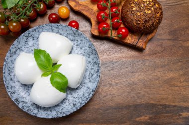 Peynir koleksiyonu, beyaz İtalyan peynirli mozzarella topları, kırmızı vişneli domates ve taze fesleğen yapraklarıyla servis ediliyor.