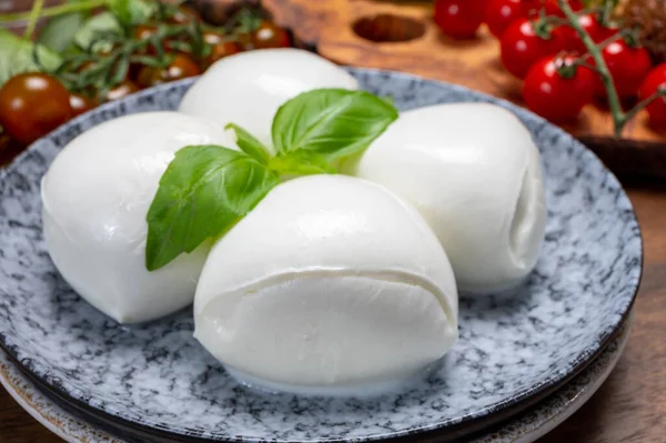Peynir koleksiyonu, beyaz İtalyan peynirli mozzarella topları, kırmızı vişneli domates ve taze fesleğen yapraklarıyla servis ediliyor.