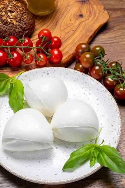 Peynir koleksiyonu, beyaz İtalyan peynirli mozzarella topları, kırmızı vişneli domates ve taze fesleğen yapraklarıyla servis ediliyor.