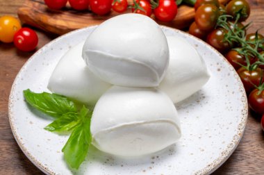 Peynir koleksiyonu, beyaz İtalyan peynirli mozzarella topları, kırmızı vişneli domates ve taze fesleğen yapraklarıyla servis ediliyor.