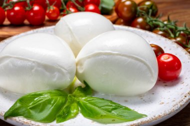 Peynir koleksiyonu, beyaz İtalyan peynirli mozzarella topları, kırmızı vişneli domates ve taze fesleğen yapraklarıyla servis ediliyor.