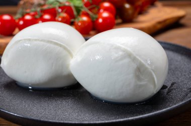 Peynir koleksiyonu, beyaz İtalyan peynirli mozzarella topları, kırmızı vişneli domates ve taze fesleğen yapraklarıyla servis ediliyor.