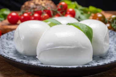 Peynir koleksiyonu, beyaz İtalyan peynirli mozzarella topları, kırmızı vişneli domates ve taze fesleğen yapraklarıyla servis ediliyor.