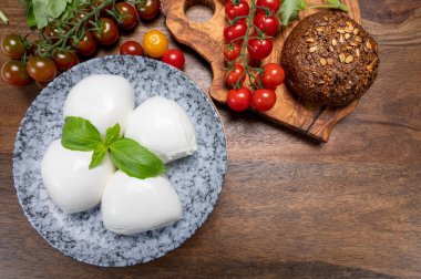 Peynir koleksiyonu, beyaz İtalyan peynirli mozzarella topları, kırmızı vişneli domates ve taze fesleğen yapraklarıyla servis ediliyor.