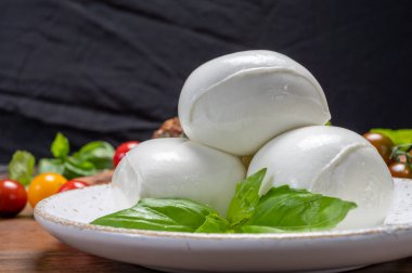 Peynir koleksiyonu, beyaz İtalyan peynirli mozzarella topları, kırmızı vişneli domates ve taze fesleğen yapraklarıyla servis ediliyor.