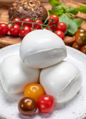 Peynir koleksiyonu, beyaz İtalyan peynirli mozzarella topları, kırmızı vişneli domates ve taze fesleğen yapraklarıyla servis ediliyor.