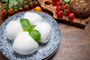 Peynir koleksiyonu, beyaz İtalyan peynirli mozzarella topları, kırmızı vişneli domates ve taze fesleğen yapraklarıyla servis ediliyor.