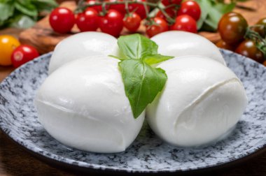 Peynir koleksiyonu, beyaz İtalyan peynirli mozzarella topları, kırmızı vişneli domates ve taze fesleğen yapraklarıyla servis ediliyor.