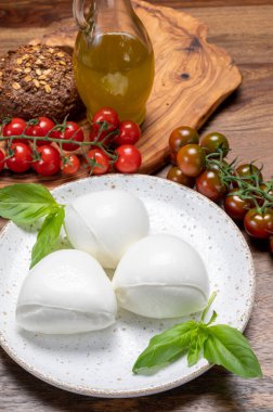 Peynir koleksiyonu, beyaz İtalyan peynirli mozzarella topları, kırmızı vişneli domates ve taze fesleğen yapraklarıyla servis ediliyor.