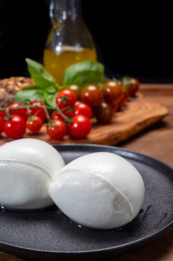 Peynir koleksiyonu, beyaz İtalyan peynirli mozzarella topları, kırmızı vişneli domates ve taze fesleğen yapraklarıyla servis ediliyor.