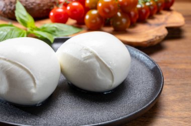 Peynir koleksiyonu, beyaz İtalyan peynirli mozzarella topları, kırmızı vişneli domates ve taze fesleğen yapraklarıyla servis ediliyor.