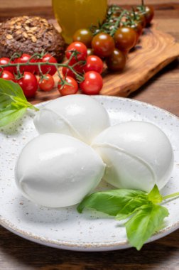 Peynir koleksiyonu, beyaz İtalyan peynirli mozzarella topları, kırmızı vişneli domates ve taze fesleğen yapraklarıyla servis ediliyor.