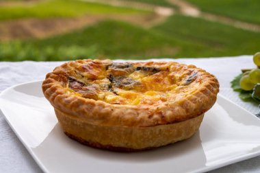 Taze pişmiş Fransız kiş sebzeli turta ve arka planda yeşil üzüm bağları.