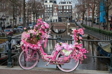 Amsterdam 'ın eski bir bölgesinde küçük bir köprüde pembe çiçeklerle süslenmiş eski model kadın bisikleti.